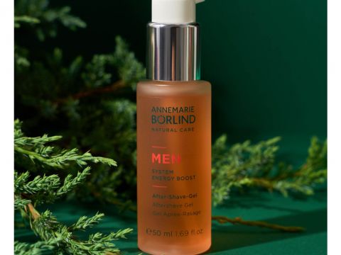 Eine Flasche Annemarie Börlind MEN System Energy Boost After Shave Gel auf grünem Hintergrund mit immergrünen Zweigen darum herum. Die Flasche ist mattiert, hat einen Pumpspender und fasst 50 ml (1,69 fl oz) Produkt.