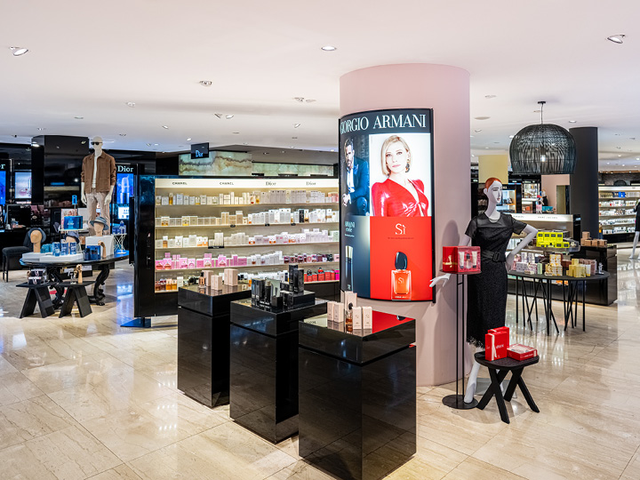 Ein Luxuskaufhaus präsentiert verschiedene Parfümmarken, darunter Giorgio Armani. Helles Licht hebt moderne schwarze Ausstellungsständer voller Produkte hervor. Im Hintergrund sind Regale mit weiteren Schönheitsartikeln gefüllt.
