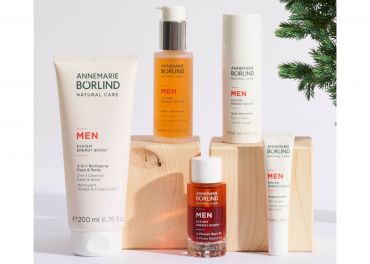 Eine Kollektion von Annemarie Börlind Hautpflegeprodukten für Männer, darunter Lotionen und Seren, angeordnet auf Holzblöcken. An der Seite ist ein kleiner immergrüner Zweig sichtbar, der der Präsentation eine natürliche Note verleiht.