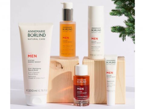 Eine Kollektion von Annemarie Börlind Hautpflegeprodukten für Männer, darunter Lotionen und Seren, angeordnet auf Holzblöcken. An der Seite ist ein kleiner immergrüner Zweig sichtbar, der der Präsentation eine natürliche Note verleiht.