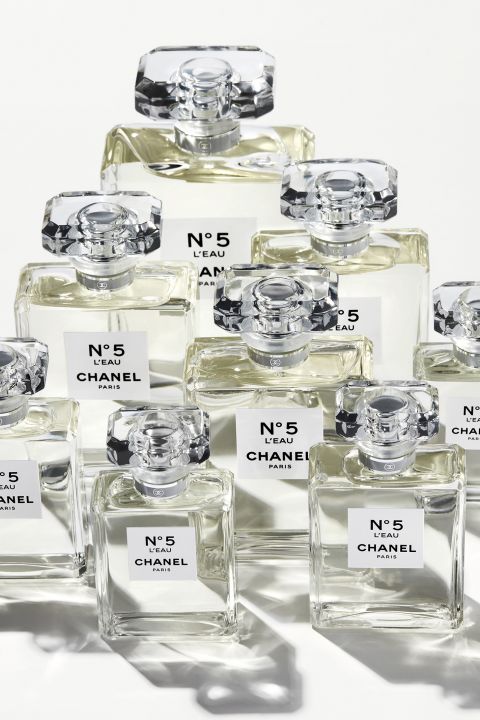 Eine Gruppe von Chanel No. 5 L'Eau-Parfümflaschen in Reihen angeordnet, in verschiedenen Größen. Jede Glasflasche hat ein unverwechselbares, elegantes Design mit facettierten Kappen und steht vor einem weißen Hintergrund.