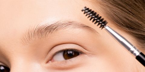 Nahaufnahme einer Person, die ihre Augenbrauen mit einer Brauenbürste pflegt. Das Auge ist geöffnet und der Fokus liegt auf der sauber geformten Braue und der Bürste, die einen silbernen Griff und schwarze Borsten hat.
