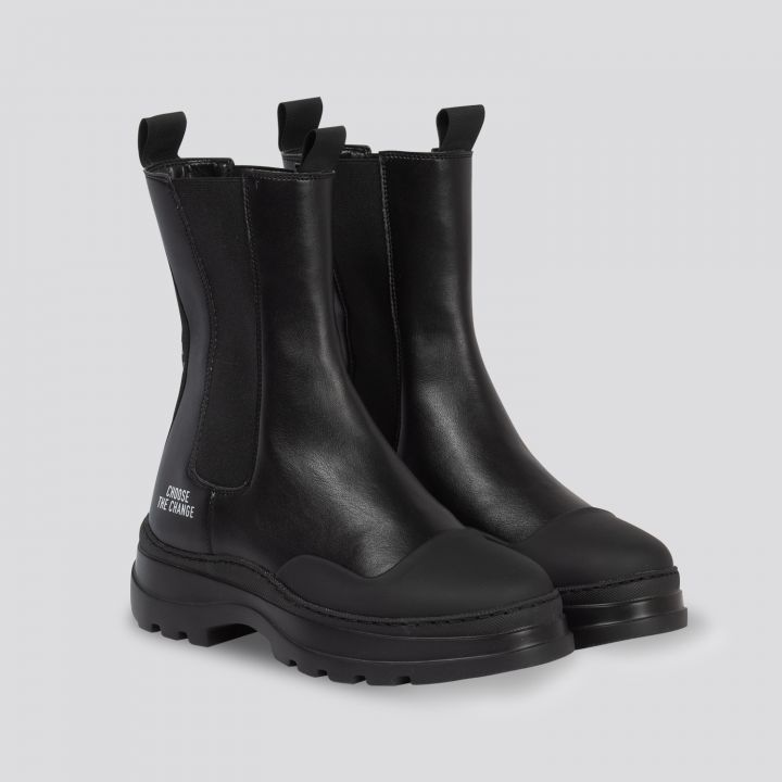 Ein Paar Chelsea-Stiefel aus schwarzem Leder mit dicker Sohle und Lasche. Die Stiefel haben eine glatte, glänzende Oberfläche und sind vor einem hellgrauen Hintergrund zu sehen.