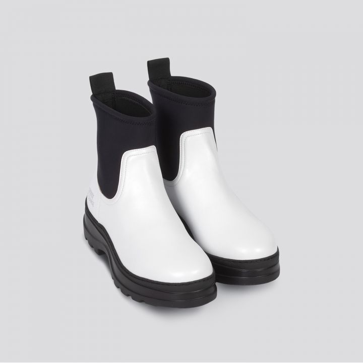 Ein Paar stylische weiße Stiefeletten mit schwarzen elastischen Einsätzen und dicken schwarzen Sohlen auf hellgrauem Untergrund.