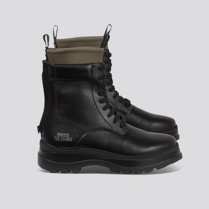 Ein Paar schwarze Leder-Kampfstiefel auf grauem Untergrund. Sie haben schwarze Schnürsenkel, eine robuste Sohle und einen grünen Textilkragen. Auf der Seite des rechten Stiefels sind die Worte „Choose the Change“ eingeprägt.