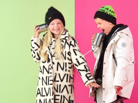 Zwei Kinder spielen mit Dosentelefonen. Das Mädchen links trägt einen gemusterten Mantel und eine schwarze Mütze und lächelt. Der Junge rechts trägt einen weißen Mantel und eine grüne Mütze und tut so, als würde er sprechen. Der Hintergrund ist in Rosa und Grün gespalten.