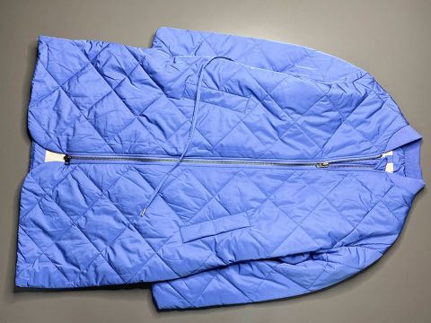 Eine blaue Steppjacke mit Reißverschluss vorne liegt flach auf einer grauen Oberfläche. Die Jacke hat ein Rautenmuster und einen Kordelzug in der Taille.