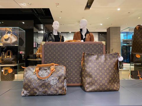 Ausstellung eines Luxusgeschäfts mit verschiedenen Louis Vuitton-Taschen, darunter ein großer Koffer, Handtaschen und eine Umhängetasche. Hinter der Ausstellung stehen zwei Schaufensterpuppen in modischen Outfits.