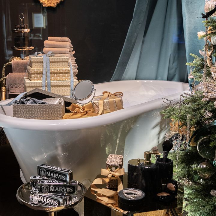 Eine dekorierte Badewanne ist von luxuriösen Badeprodukten und Toilettenartikeln umgeben. Daneben steht ein mit Ornamenten geschmückter Weihnachtsbaum. Handtücher und Badeaccessoires sind ordentlich angeordnet und schaffen eine festliche und opulente Atmosphäre.