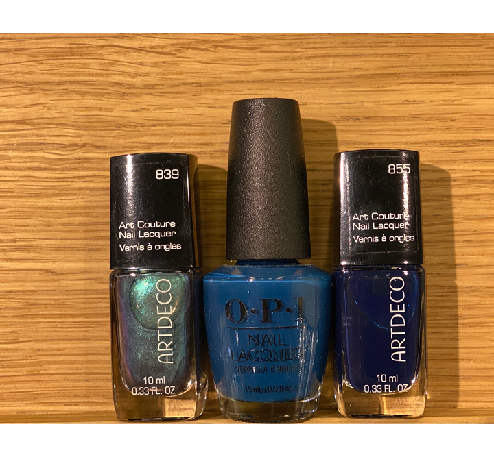 Drei Nagellackflaschen werden auf einer Holzoberfläche ausgestellt. Die Farben sind schillerndes Grün, leuchtendes Blau und tiefes Marineblau. Die mittlere Flasche ist von OPI und die anderen sind von Artdeco.