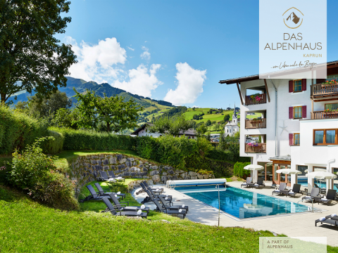 Eine malerische Aussicht auf das Alpenhaus Kaprun, ein modernes Hotel mit Balkonen, einem Swimmingpool umgeben von Liegestühlen und üppigen grünen Hügeln mit Bäumen im Hintergrund unter einem klaren blauen Himmel.