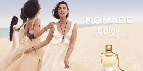 Vier Frauen gehen in wallenden Kleidern durch eine Wüstenlandschaft. Rechts sind der Text „Nomade Chloé“ und eine Parfümflasche zu sehen, die für den Duft wirbt. Die Szene vermittelt ein Gefühl von Freiheit und natürlicher Eleganz.