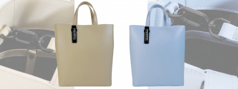 Ausgestellt werden zwei Handtaschen: eine beige und eine hellblau. Jede hat einen schwarzen Verschluss und Griff, an dem ein kleines schwarzes Etikett befestigt ist. Der Fokus liegt auf ihrem Design und ihren Details.