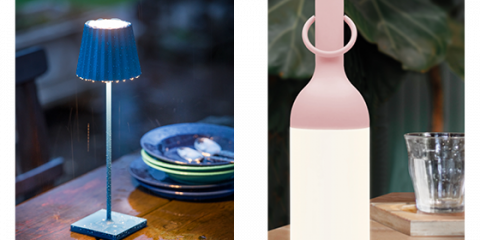Gezeigt werden zwei Lampen: eine blaue Tischlampe im Außenbereich, an deren Schirm Regentropfen herabprasseln, und eine rosafarbene, flaschenförmige Lampe, die im Innenbereich neben einem klaren Glas auf einer Holzoberfläche sanft leuchtet.