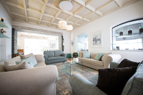 Ein gemütliches Wohnzimmer mit einer plüschigen Sitzgruppe in Beige und Blau. Der Raum verfügt über einen Couchtisch aus Glas, eine Topfpflanze, sanfte Beleuchtung, eine helle Holzdecke und zeitgenössisches Dekor, was eine einladende und stilvolle Atmosphäre schafft.