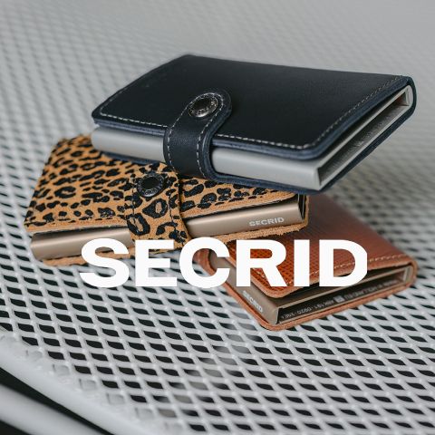 Drei Secrid-Geldbörsen - schwarz, mit Leopardenmuster und braun - sind auf einer weißen Metalloberfläche gestapelt und mit dem Text SECRID" in fetten weißen Buchstaben überlagert.