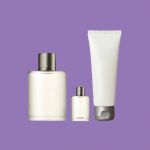 Eine Sammlung von drei weißen Pflegeprodukten vor violettem Hintergrund: eine große Sprühflasche mit silberner Kappe, eine kleine Flasche mit Deckel und eine Tube mit silberner Kappe.