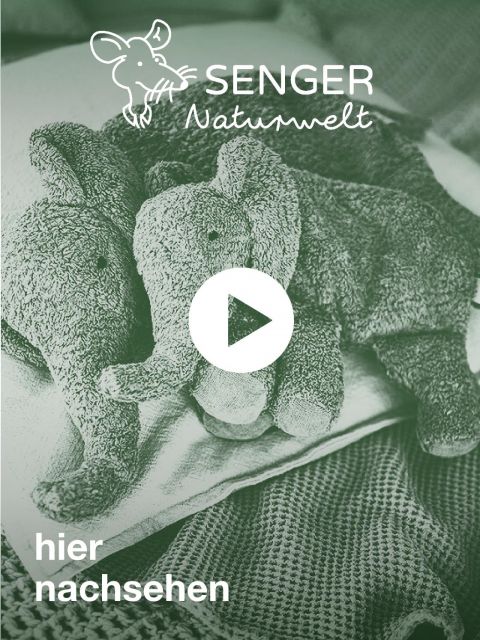 Ein monochromes Bild von zwei strukturierten Plüschelefanten, die auf einem Bett liegen. Der Text „Senger Naturwelt“ und „hier nachsehen“ ist sichtbar, zusammen mit einer Überlagerung mit einem Play-Button-Symbol.