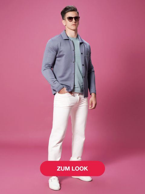 Ein Mann steht selbstbewusst vor einem rosa Hintergrund, trägt eine Sonnenbrille, eine blaugraue Jacke über einem grünlich-grauen Hemd, eine weiße Hose und weiße Turnschuhe. Unten in der Mitte befindet sich ein roter Button mit dem Text „Zum Look“.