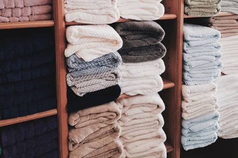 Stapel ordentlich gefalteter Handtücher in verschiedenen Farben, darunter Weiß, Beige, Grau und Blau, sind auf Holzregalen angeordnet.