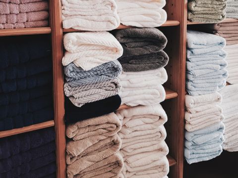 Stapel ordentlich gefalteter Handtücher in verschiedenen Farben, darunter Weiß, Beige, Grau und Blau, sind auf Holzregalen angeordnet.