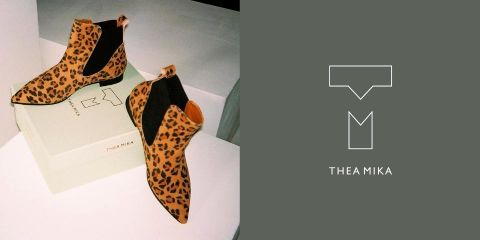 Auf einem hellgrünen Schuhkarton ist ein Paar Stiefeletten mit Leopardenmuster abgebildet. Der Hintergrund ist grün und trägt auf der rechten Seite „Thea Mika“ und ein Logo.