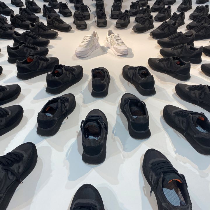 Eine Sammlung schwarzer Schuhe ist in kreisförmigen Mustern auf einer weißen Oberfläche angeordnet, wobei zwei weiße Schuhe in der Mitte platziert sind und einen kontrastierenden Blickfang bilden.