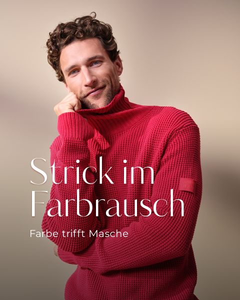 Ein Mann mit lockigem Haar trägt einen dicken roten Rollkragenpullover und lächelt sanft, eine Hand am Kinn. Der deutsche Text auf dem Bild lautet: "Strick im Farbrausch. Farbe trifft Masche.".