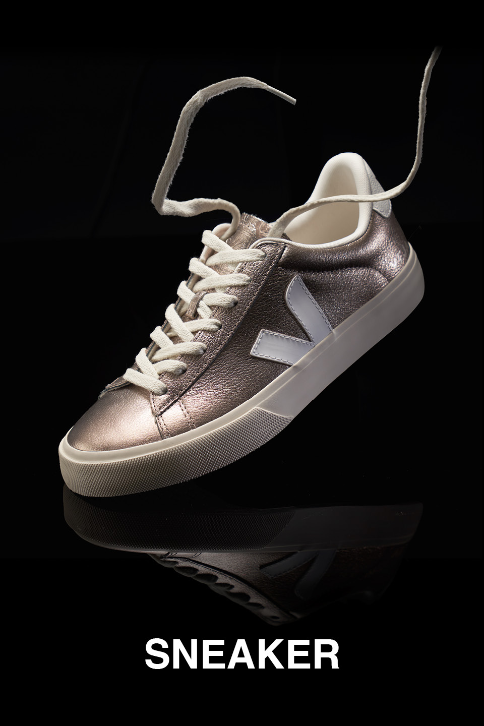 Ein einzelner metallisch-silberner Sneaker mit weißen Schnürsenkeln und dicker Sohle schwebt vor einem schwarzen Hintergrund. Unter dem Schuh steht in fetten weißen Buchstaben das Wort „SNEAKER“.