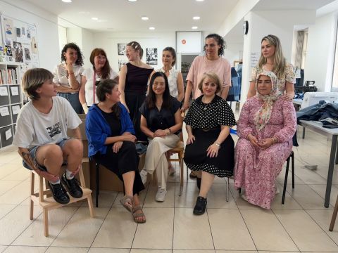 Elf Frauen unterschiedlichen Alters sitzen und stehen beieinander, lächeln und unterhalten sich in einem hellen, modernen Raum, in dessen Hintergrund Fotos, Regale und Schreibtische zu sehen sind.