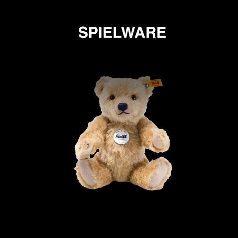 Ein Steiff Teddybär mit einer gelben Marke im Ohr sitzt vor schwarzem Hintergrund. Über dem Bären steht in weißer Schrift „SPIELWARE“.