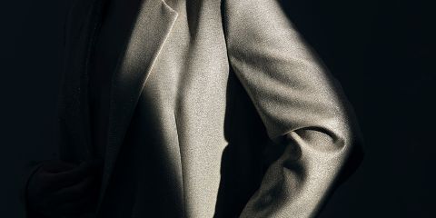 Nahaufnahme einer Person, die eine schimmernde silberne Jacke trägt, die vor einem dunklen Hintergrund teilweise von Licht beleuchtet wird. Die Textur des Stoffes ist deutlich erkennbar und hebt den Glanz und die Falten des Materials hervor.