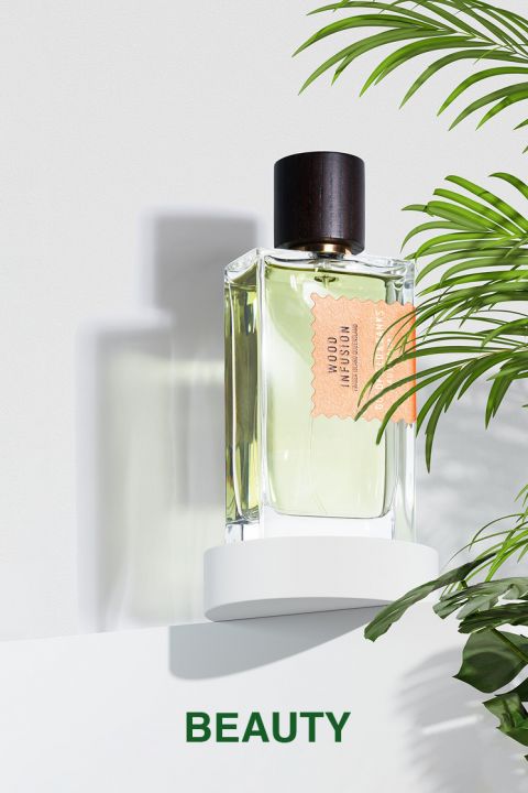 Ein durchsichtiges Parfümfläschchen aus Glas mit dunklem Deckel und dem Etikett „Melon Skin Cologne“ steht auf einer weißen Fläche, umgeben von grünen Blättern. Am unteren Bildrand ist das Wort „BEAUTY“ aufgedruckt.
