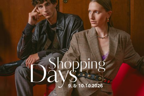 Zwei modisch gekleidete Personen sitzen auf roten Möbeln vor einer Holzvertäfelung. Der Text lautet: „Shopping-Tage 9. und 10.10.2026.“.
