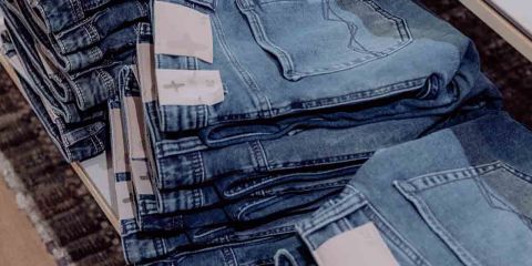 Stapel gefalteter Blue Jeans auf dem Display, mit sichtbaren Gesäßtaschen und Etiketten. Die Jeans sind ordentlich in Spalten auf einem Ladenregal angeordnet.