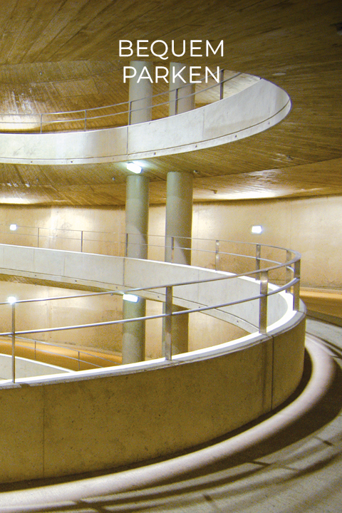 Spiralförmige Rampe eines Parkhauses mit strukturiertem Beton und Metallgeländern. Deckenleuchten beleuchten die Kurven. Oben steht in weißer Schrift der Schriftzug „BEQUEM PARKEN“.
