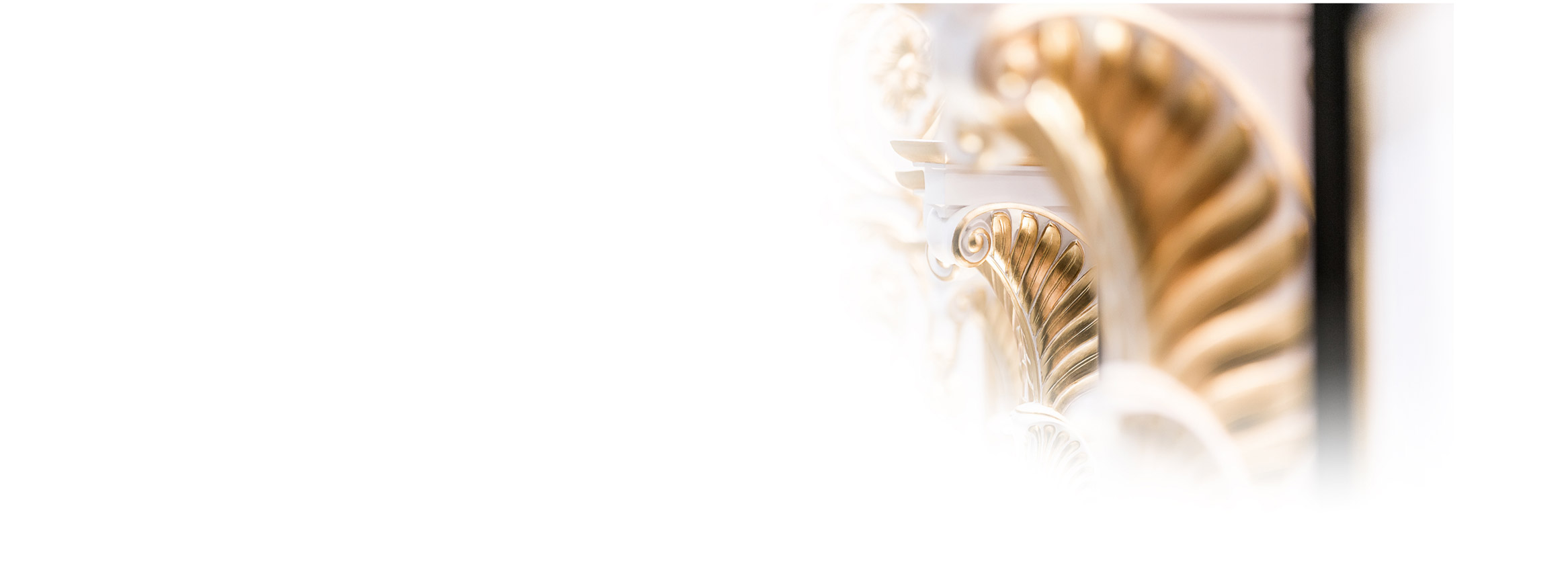 Nahaufnahme von kunstvollen, goldenen Architekturdetails mit Unschärfeeffekt. Das Design zeigt komplizierte Spiralformen auf weißem Hintergrund.