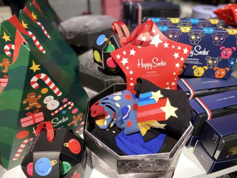 Eine Auswahl an Socken-Geschenksets mit festlichen Motiven, farbenfrohen Mustern mit Sternen und Streifen. Die Verpackung enthält Weihnachtsbäume, Zuckerstangen und Bären sowie ein „Happy Socks“-Etikett in einer sternförmigen Schachtel.