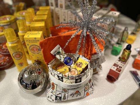 Ein festliches Arrangement mit L'Occitane-Produkten, darunter Lotionen, Sprays und Toilettenartikel in leuchtenden Verpackungen. Das Display enthält einen dekorativen silbernen Stern und ein glänzendes silbernes Ornament auf einer weißen Oberfläche.