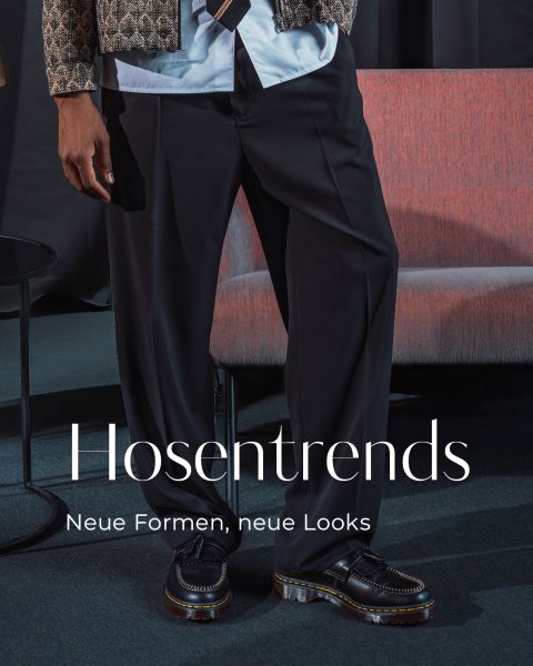 Eine Person in schwarzer Hose und Slippern steht neben einem roten Sessel. Der Text lautet: „Hosentrends. Neue Formen, neue Looks.“.