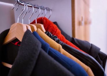 Eine Reihe Wintermäntel in verschiedenen Farben, darunter Schwarz, Blau, Braun und Rot, hängen ordentlich auf Holzbügeln in einem Kleiderschrank.