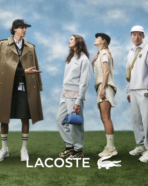 Vier Models posieren im Freien in Lacoste-Outfits vor einem blauen Himmel. Von links nach rechts: eine Person im Trenchcoat, eine Person in Pullover und Hose, eine Person in Weste und Rock und eine Person im Trainingsanzug. Das Lacoste-Logo befindet sich unten.