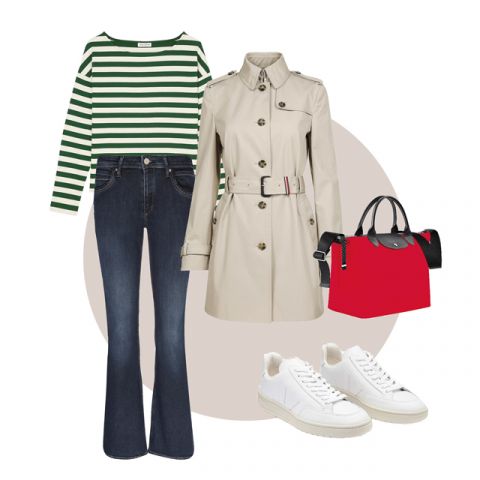Ein stylisches Outfit bestehend aus einem grün-weiß gestreiften Langarmshirt, einem beigen Trenchcoat, dunkelblauen Schlagjeans, weißen Sneakers und einer roten Handtasche mit schwarzen Akzenten. Das Ensemble ist auf einem neutralen Hintergrund arrangiert.