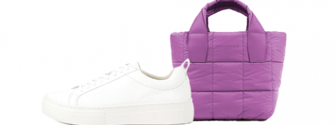 Eine Nahaufnahme eines weißen Sneakers mit Schnürsenkeln neben einer kleinen lila gesteppten Handtasche mit Griffen.