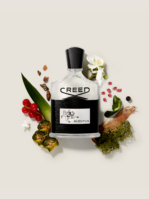 Eine Glasflasche mit Creed Aventus-Parfüm, umgeben von seinen Inhaltsstoffen: rote Beeren, weiße Blumen, Ananas, Moos und einige dunkle Gewürze. Der Hintergrund ist in einem sanften Beige gehalten.