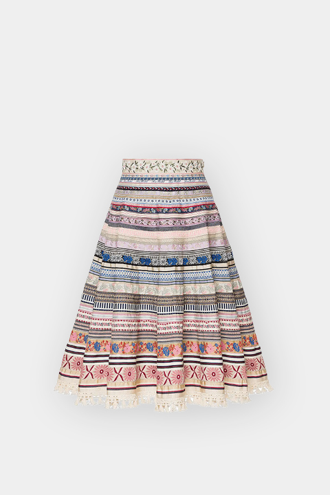 Ein knielanger Rock in A-Linie mit bunten Querstreifen, verschlungenen Mustern und Blumenstickereien auf weißem Grund.
