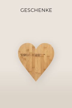 Ein herzförmiges Schneidebrett aus Holz mit eingraviertem deutschen Text. Der Hintergrund ist hellcremefarben, und oben ist das Wort „GESCHENKE“ fett gedruckt.