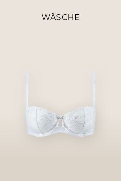 Ein weißer Spitzen-BH mit dünnen Trägern und zarter Blumenstickerei auf den Cups. Der Hintergrund ist in zartem Beige gehalten, oben ist in schwarzer Schrift „WÄSCHE“ zu lesen.