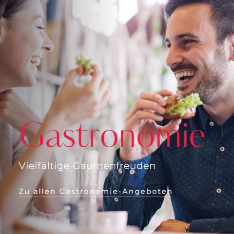Ein lächelnder Mann und eine lächelnde Frau genießen das Essen an einem Tisch. Auf der Texteinblendung steht „Gastronomie: Vielfältige Gaumenfreuden. Zu allen Gastronomie-Angeboten.