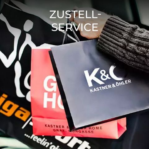 Nahaufnahme einer Hand, die mehrere Einkaufstüten hält, darunter eine rote Tüte mit der Aufschrift „GO HOME“ und eine schwarze mit der Aufschrift „K&C Kastner & Öhler“. Im oberen Teil des Bildes steht der Text „ZUSTELL-SERVICE“.
